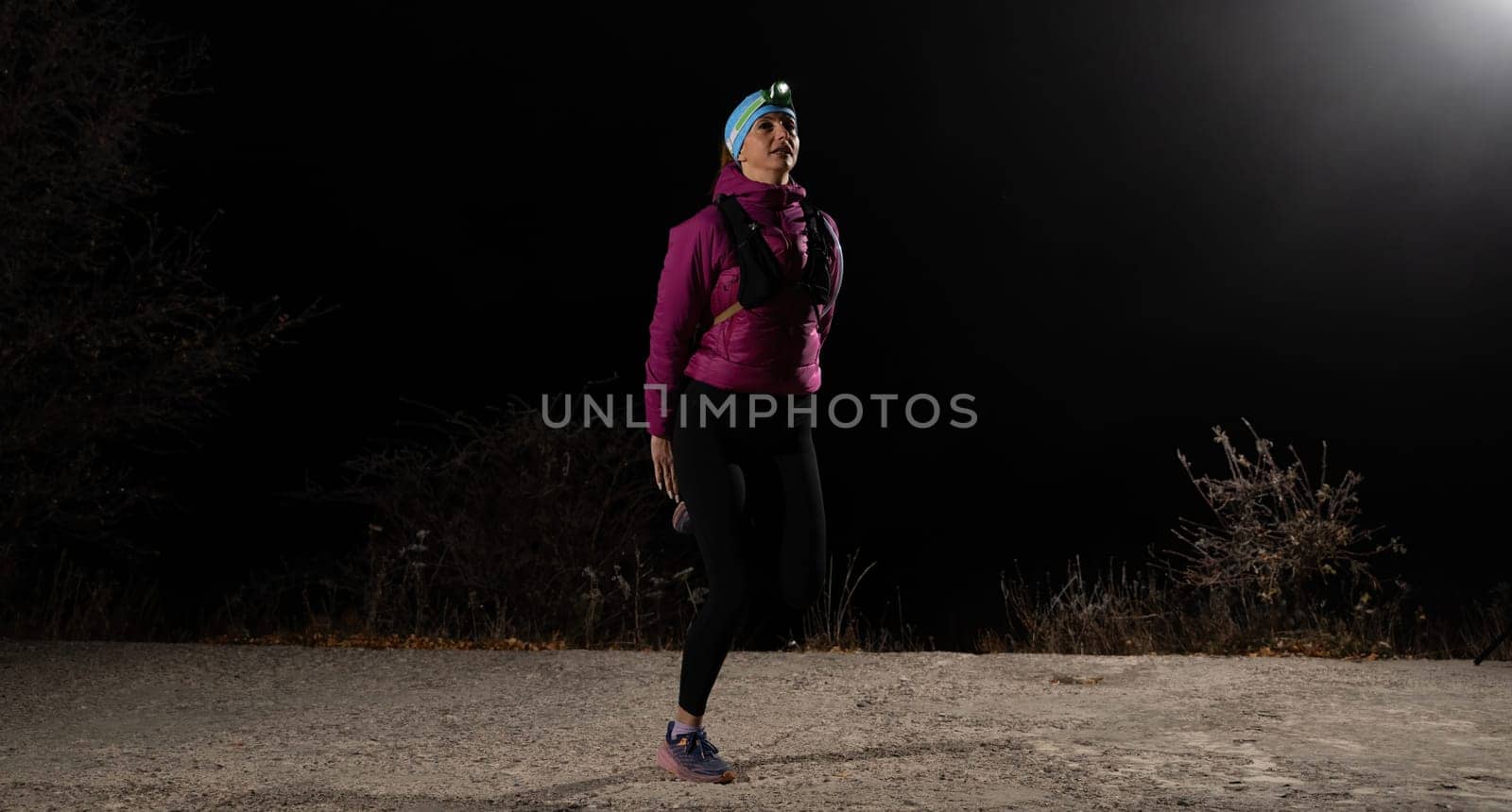 Woman jogging at night with headlamp on, captured in dark outdoor environment.