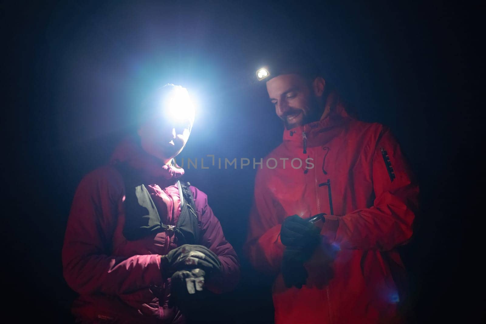 Couple night hikers examine a device under headlamp light, emphasizing navigation and teamwork under low light conditions.