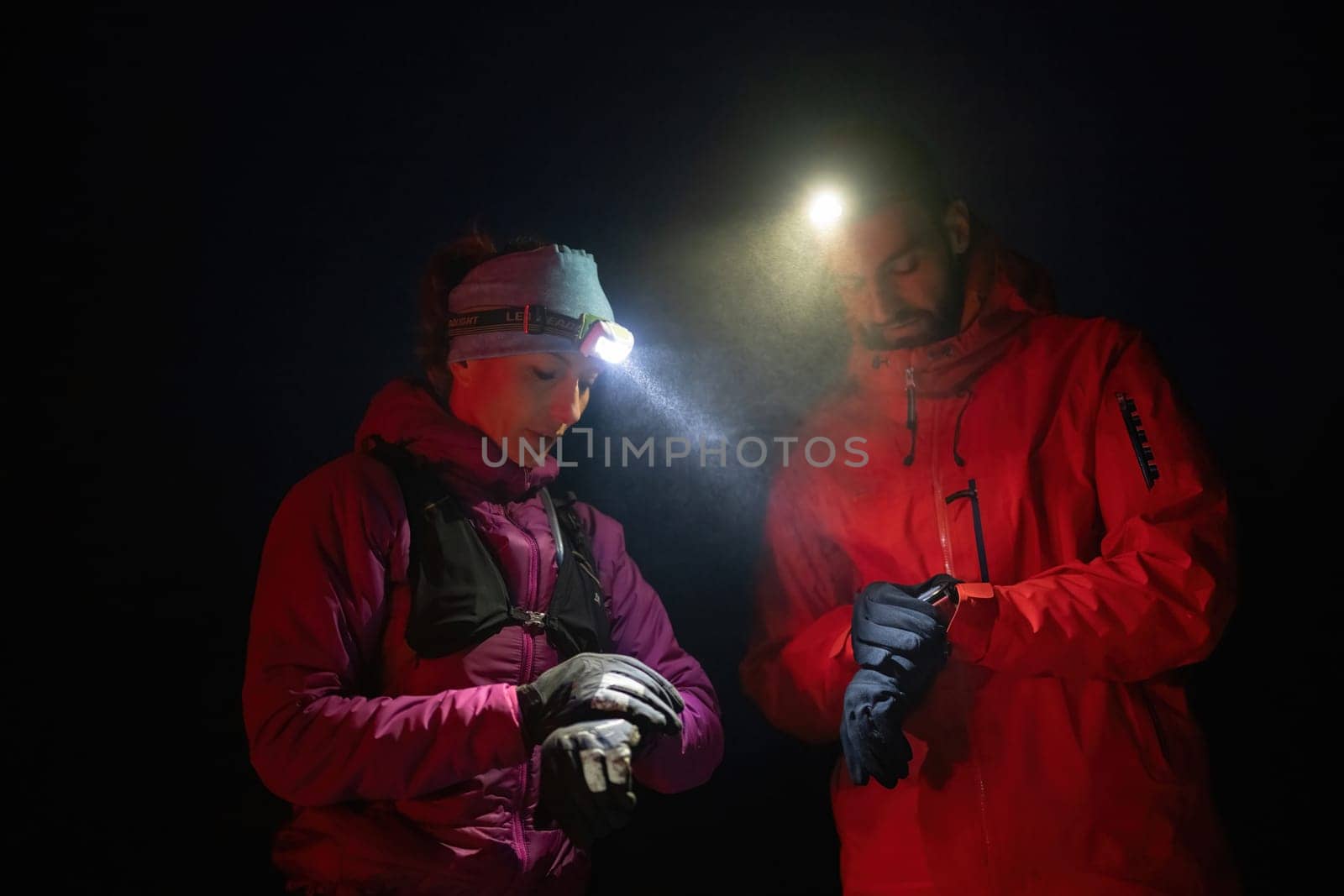 Couple night hikers examine a device under headlamp light, emphasizing navigation and teamwork under low light conditions.
