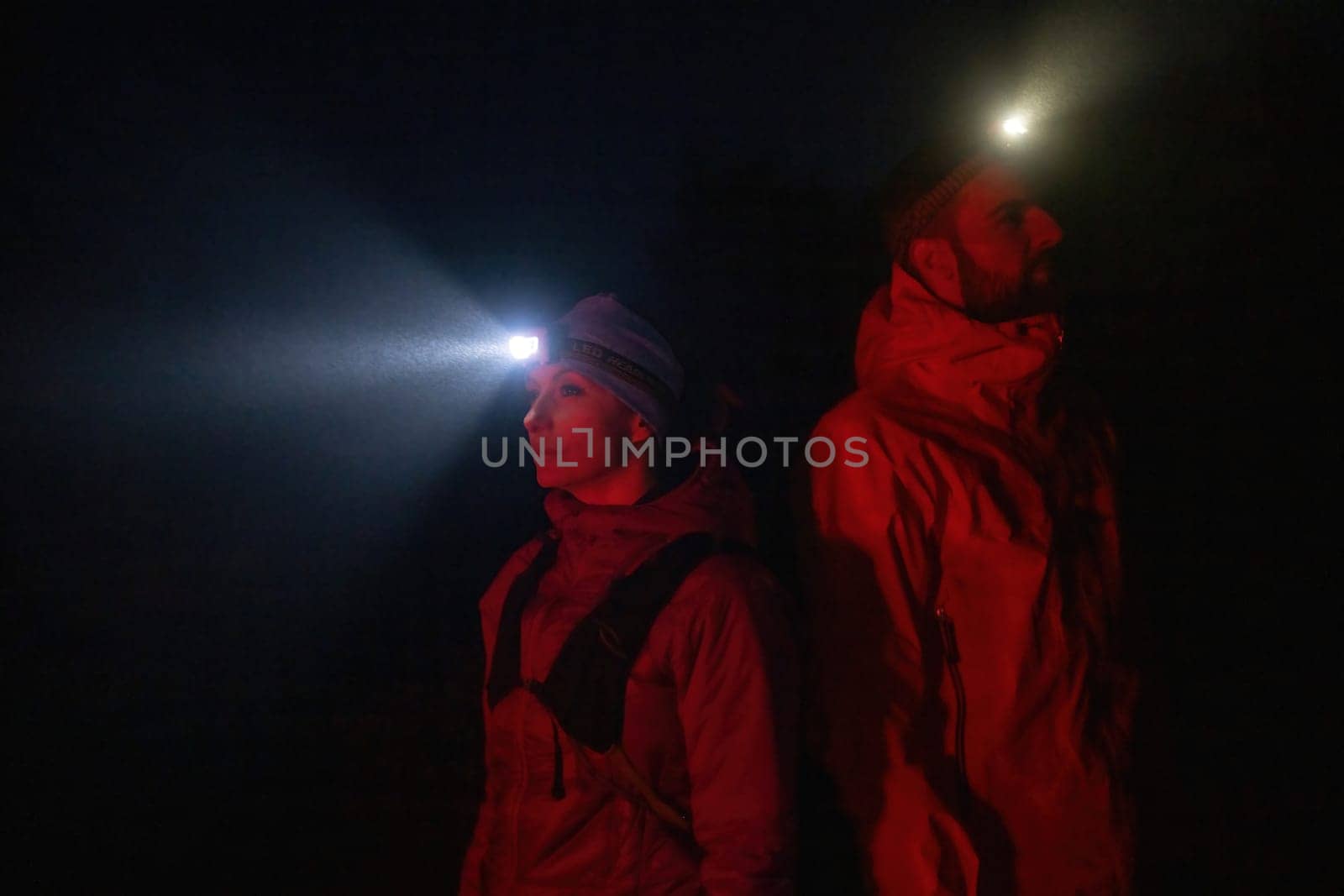 Couple equipped with headlamps explore a forest in total darkness, with beams of light cutting through the night air.