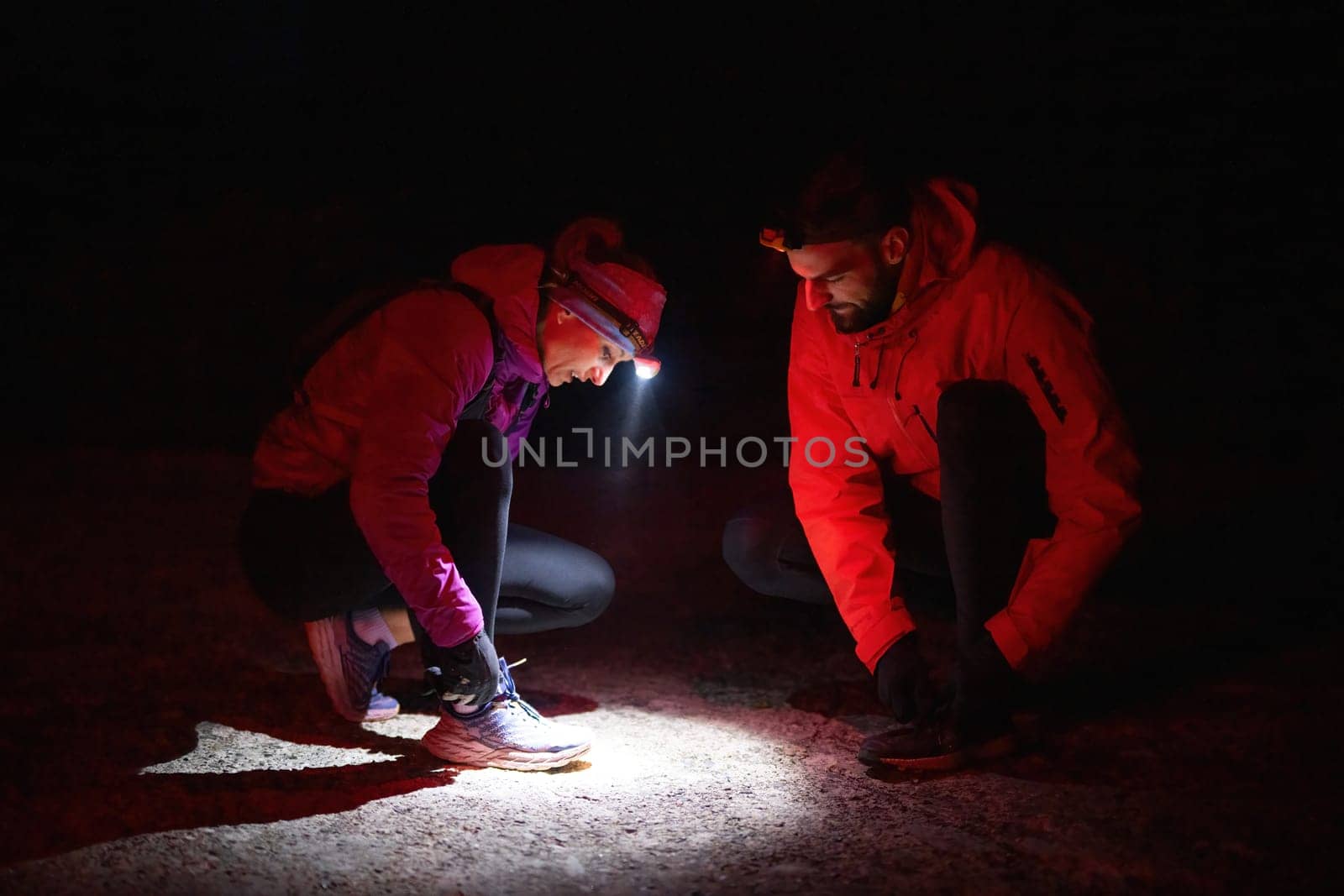 Two trekkers inspect their shoes using headlamps during a night hike, emphasizing safety and preparation in the dark.