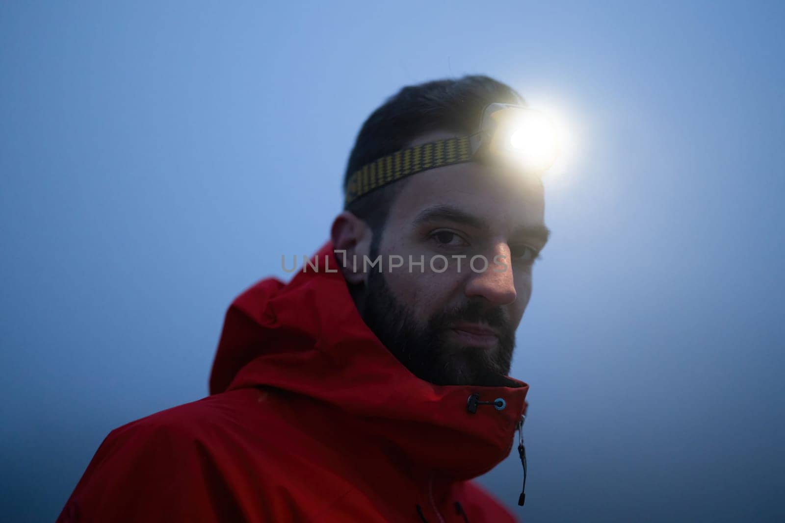 A lone hiker balances on a rocky mountain trail during early morning or dusk, with a headlamp lighting the misty path.
