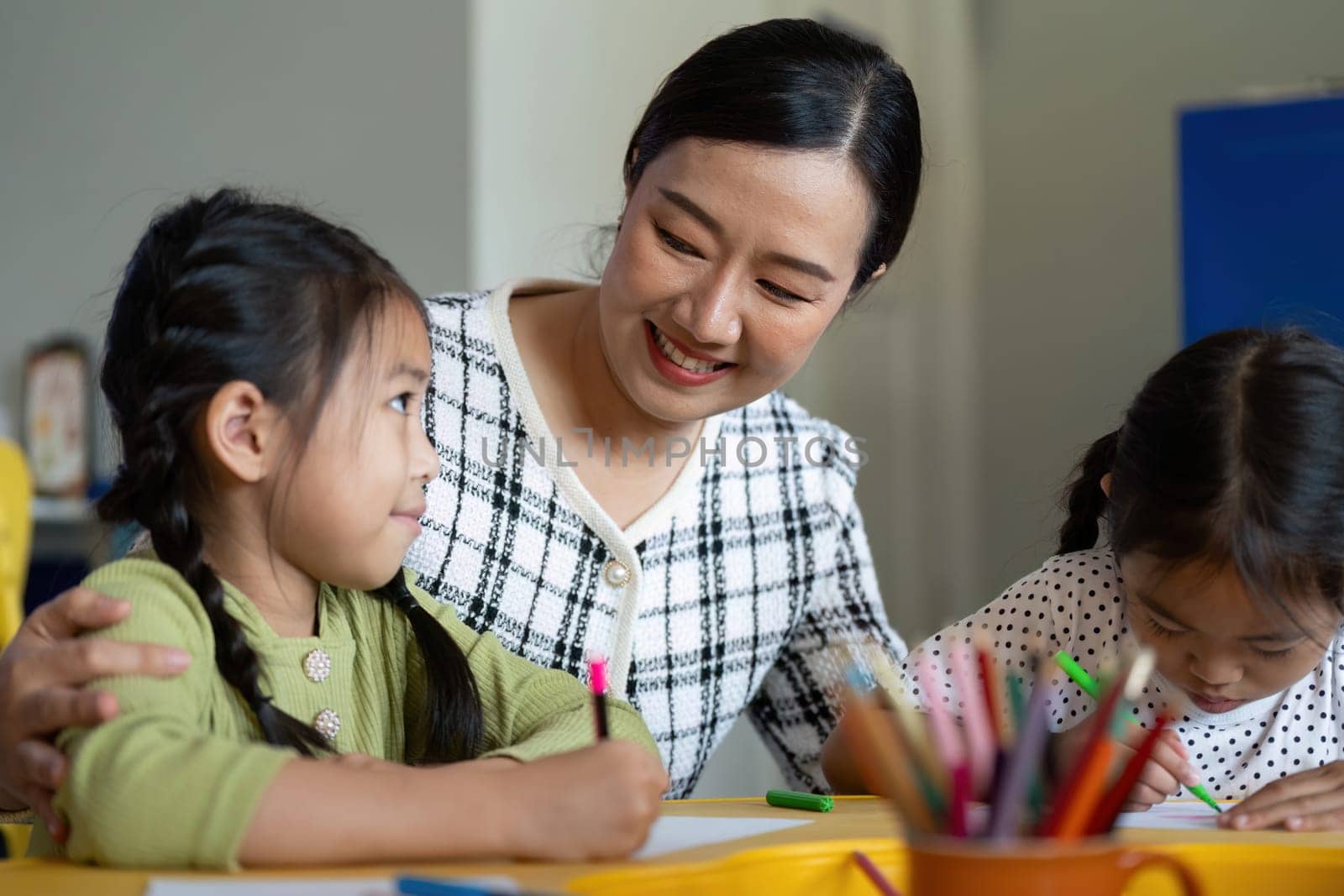 A teacher interacts warmly with young students as they enjoy a creative drawing session, fostering a love for learning.