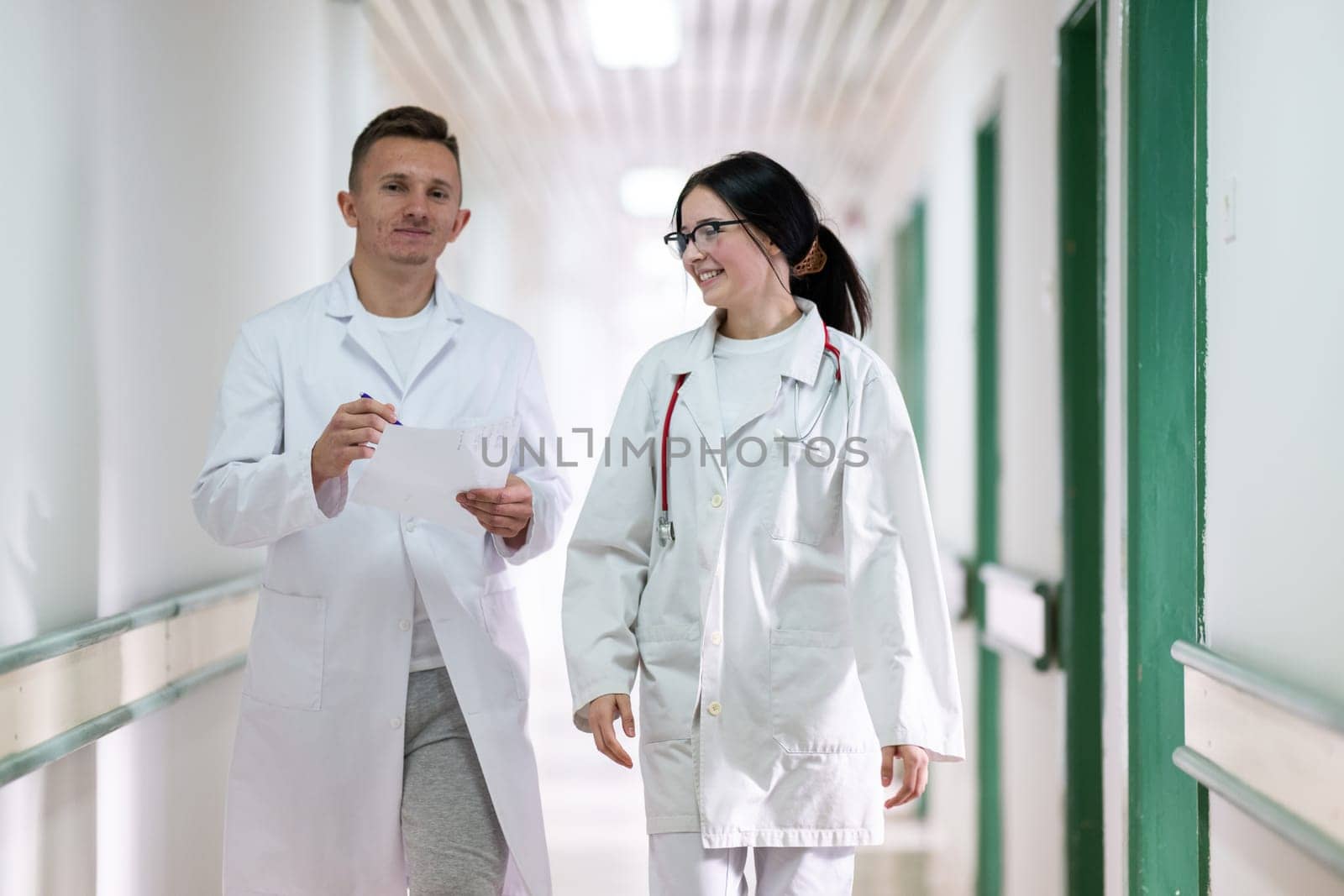 Two doctors in white coats walking and discussing medical documents in a brightly lit hospital corridor, emphasizing teamwork and professional healthcare environment.
