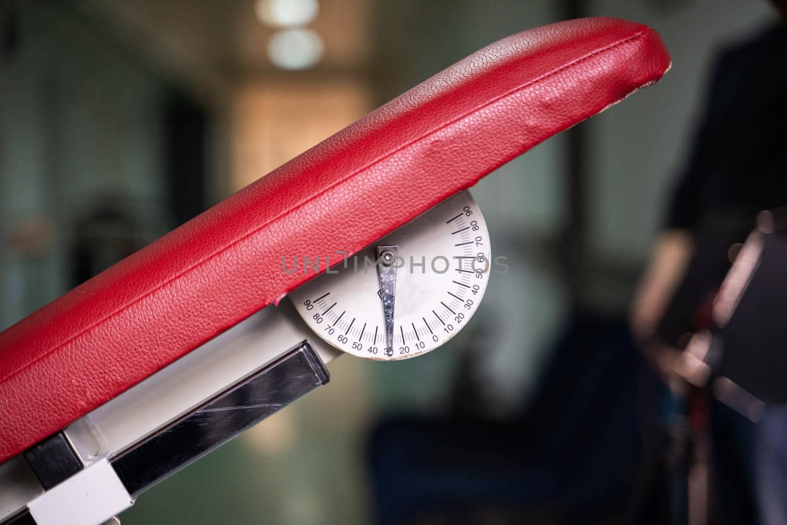 Detailed view of adjustable red physiotherapy table, showing mechanical angle indicator used in rehabilitation settings.