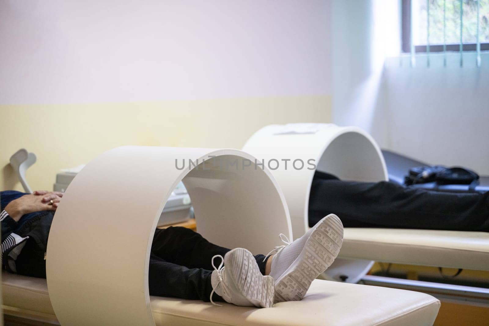 Patients lying down with legs inside circular magnetic therapy devices during a physiotherapy session.