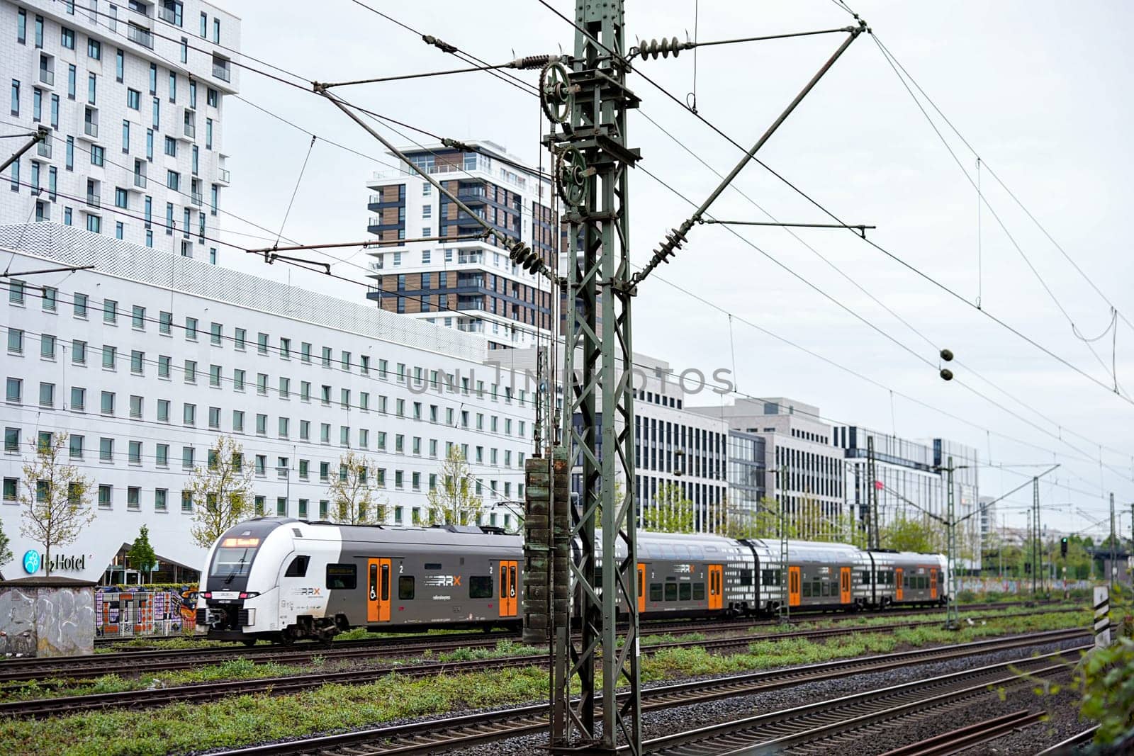 Dusseldorf, Germany 05.22.2025 Double decker commuter train rides along electrified railway tracks with contemporary high rise buildings in the background on a cloudy day