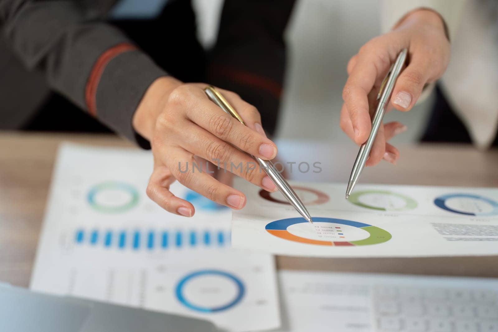 Close-up of hands pointing at data charts and reports, illustrating teamwork and analysis in a business environment.