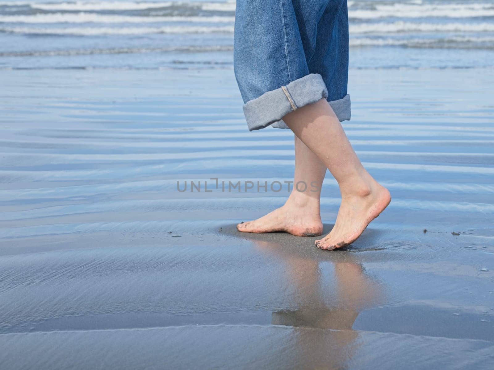 A closeup conceptual photos of a woman's feet shown barefooted walking on the beach by the pacific ocean in Washington.