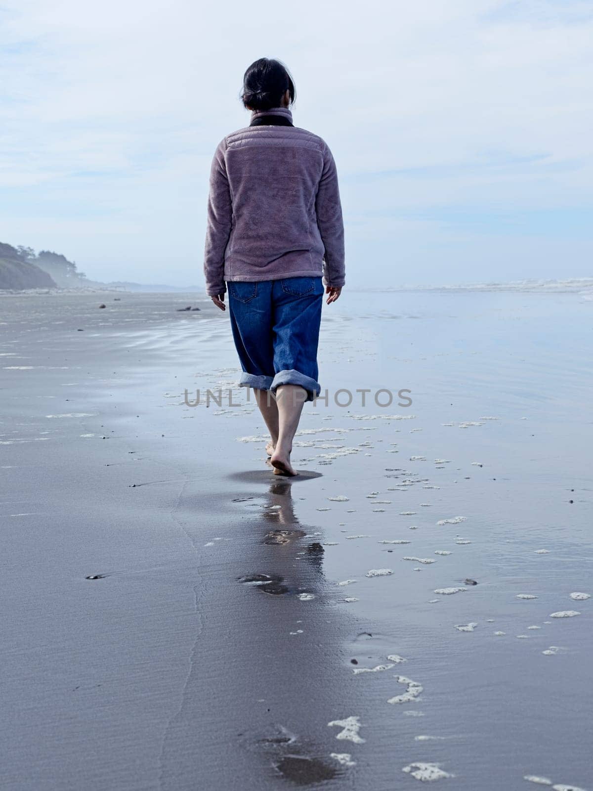 A woman walks barefooted on the beach on a sunny day along the coast of Washington State.