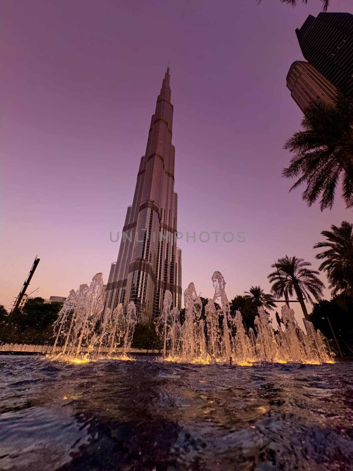 UAE, Dubai, 19 September 2024: The famous Burj Khalifa skyscraper at dusk, fountain, Dubai's sights during the incredible sunset sky, skyscrapers illuminated at night, pink sky, palm trees. High quality photo