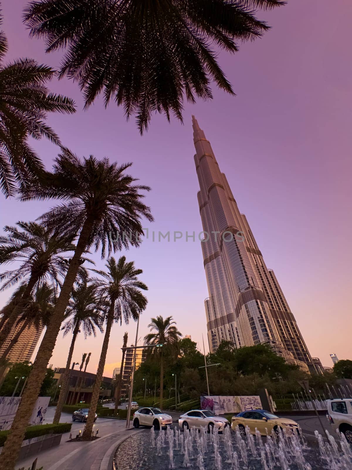 UAE, Dubai, 19 September 2024: The famous Burj Khalifa skyscraper at dusk, fountain, Dubai's sights during the incredible sunset sky, skyscrapers illuminated at night, pink sky, palm trees. High quality photo