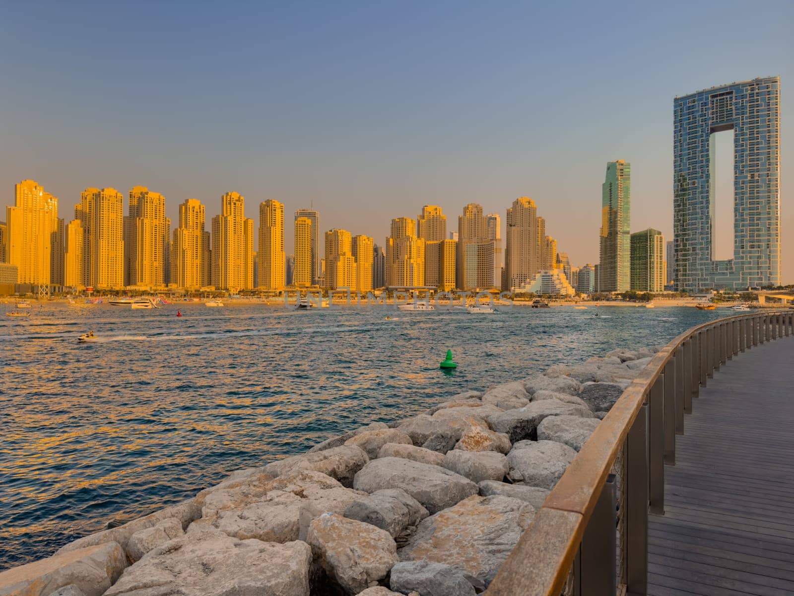 UAE, Dubai, 21 September 2024: Lively navigation of Dubai Marina along the waterfront against the backdrop of the beach and skyscrapers at sunset, boats and yachts with people on board. High quality photo