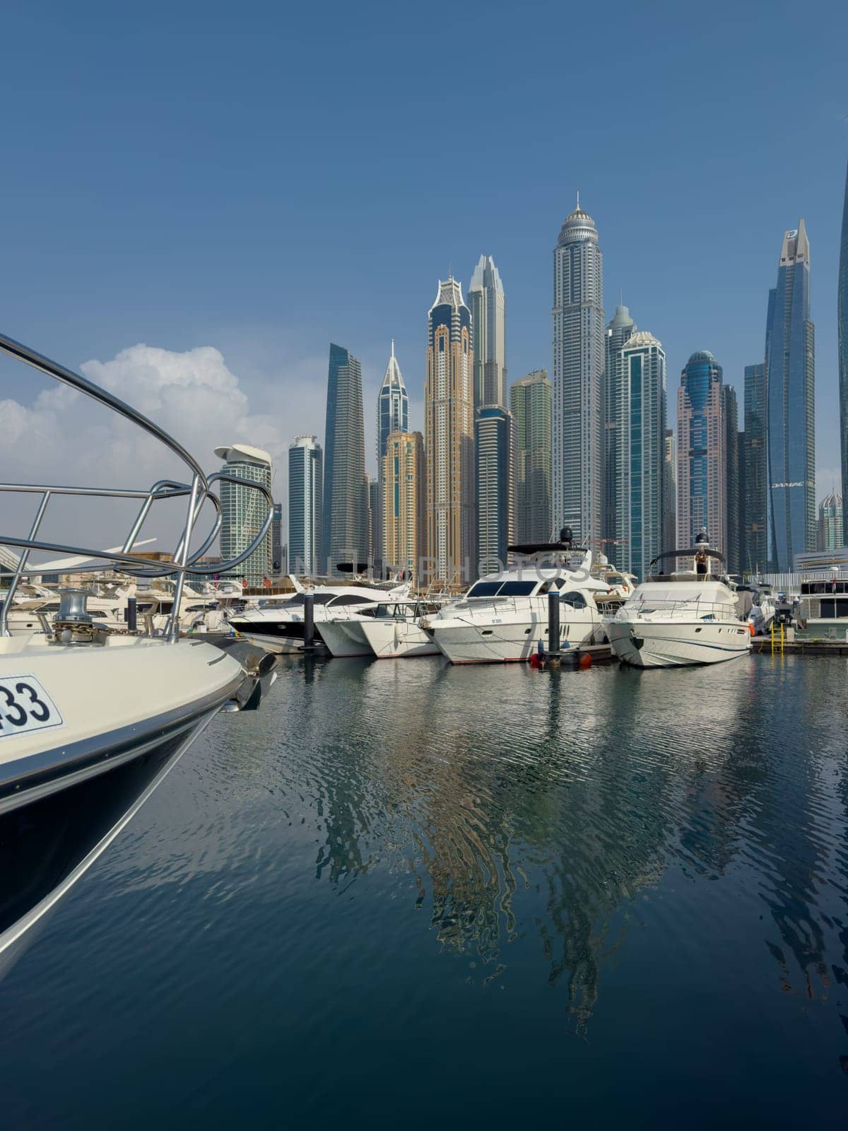 UAE, Dubai, 29 September 2024: Skyscrapers from Dubai harbor marina at sunny day, luxury yachts and boats are moored in port. High quality photo