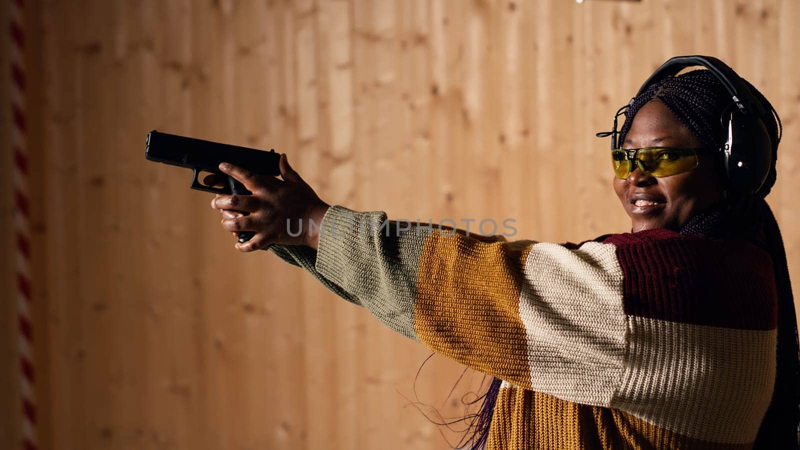Cheerful woman in shooting range trying out new gun model before committing to purchase. Happy person in firing range learning how to operate new weapon safely during self defense training, camera B