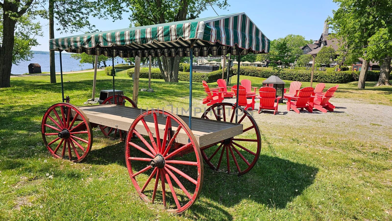 Ottawa, ON Canada - 06.04.2023: Vintage Wagon with Striped Canopy and Red Chairs in a Tranquil Lakeside Setting, Summer Day.