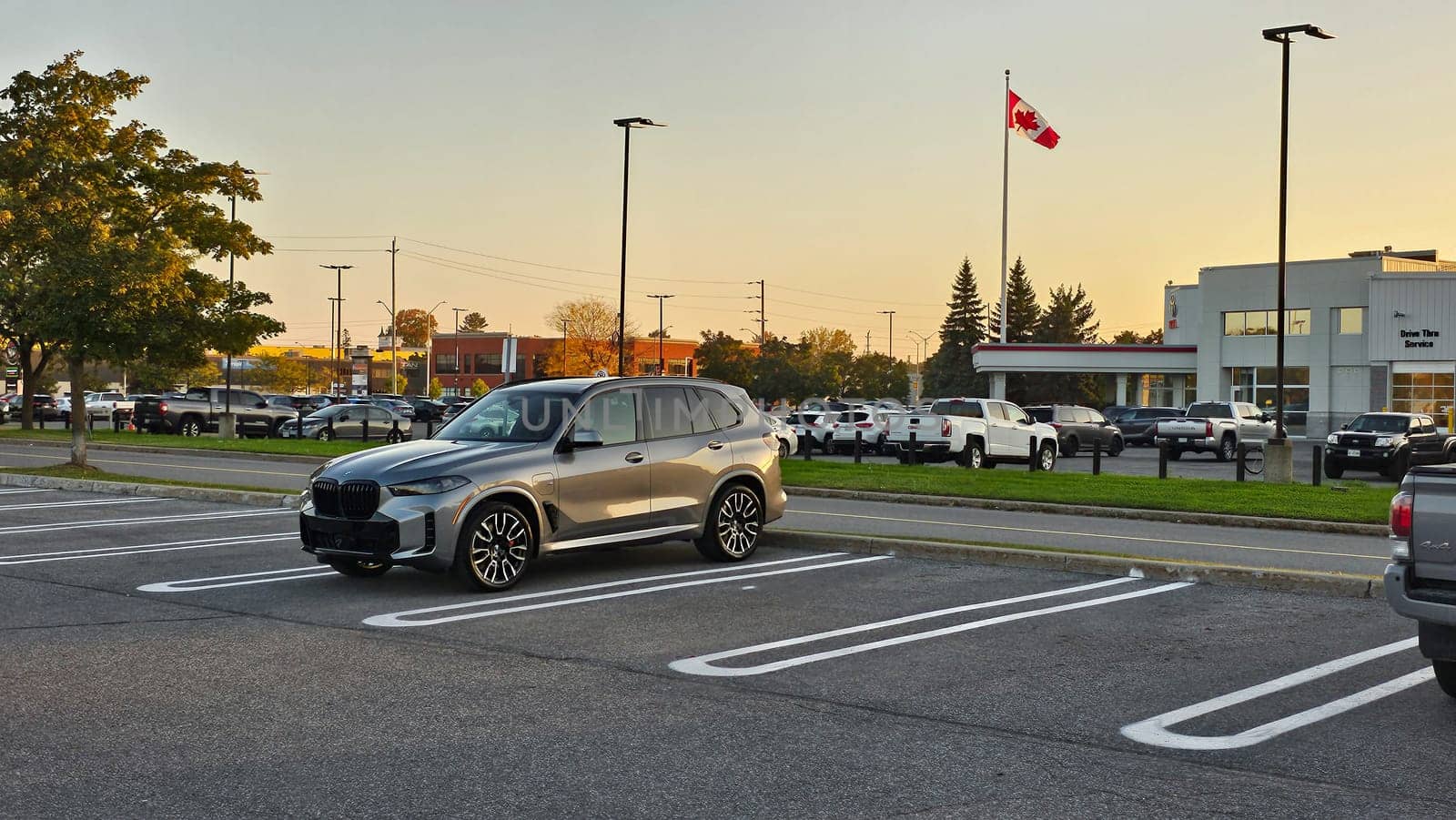 Ottawa, ON Canada - 10.04.2023: Silver BMW X5 SUV Parked in a Car Dealership Parking Lot on a Sunny Day, Canada Flag in Background.
