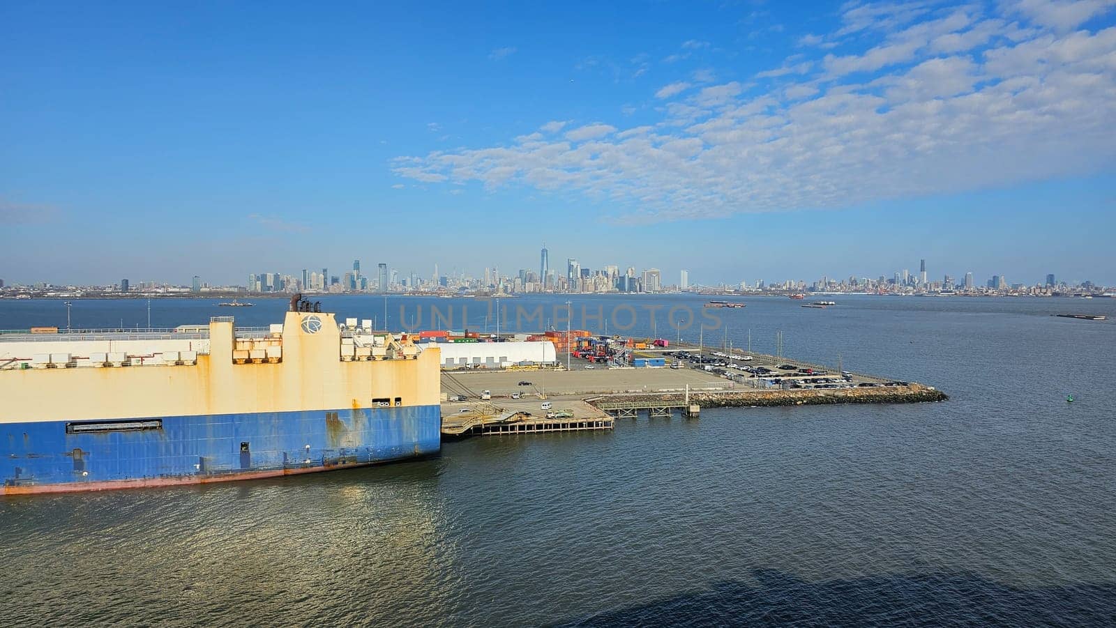 New York, NY USA - 02.09.2024: Cargo Ship Docked with Distant City Skyline Views Amidst Clear Skies And Waters.