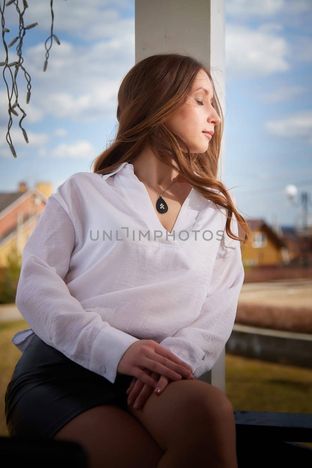 Soft sunlight illuminates a young woman sitting on a porch, captured in a tranquil moment of peaceful reflection.