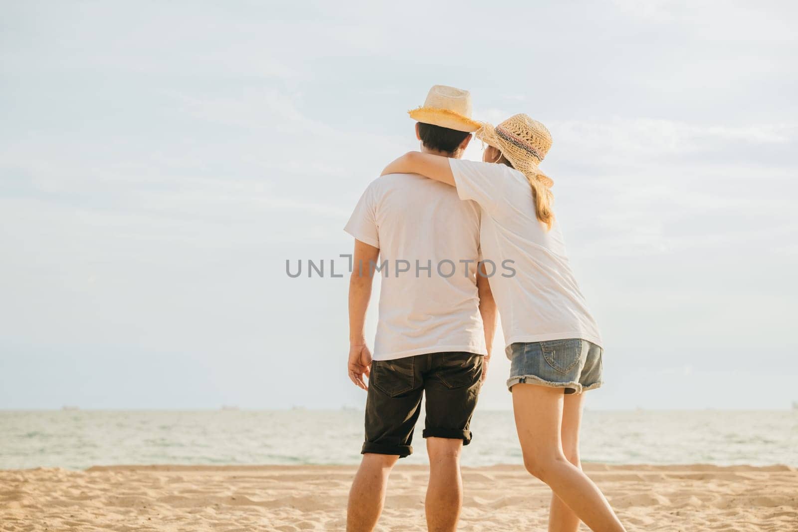 Back Asian couple standing hugging together on the beach, Happy young woman embracing her boyfriend seaside honeymoon vacation background, couple in love resting on sea