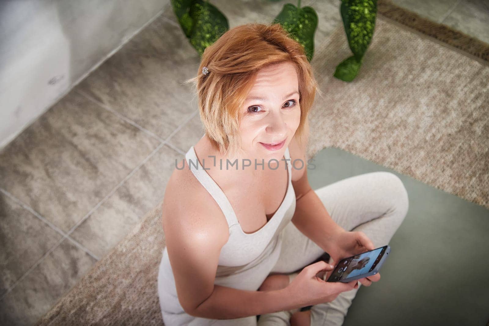 A person seated in a serene yoga space, participating in a wellness routine, connecting with a community via smartphone.