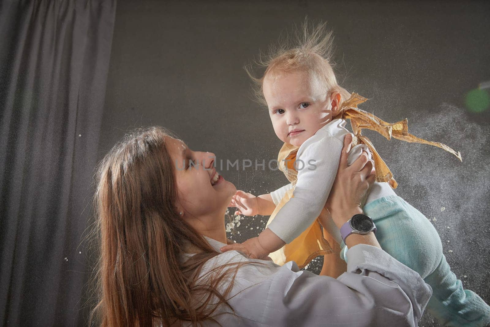 A mother and daughter joyfully engage in a flour-filled moment, creating memories in a cozy kitchen setting.