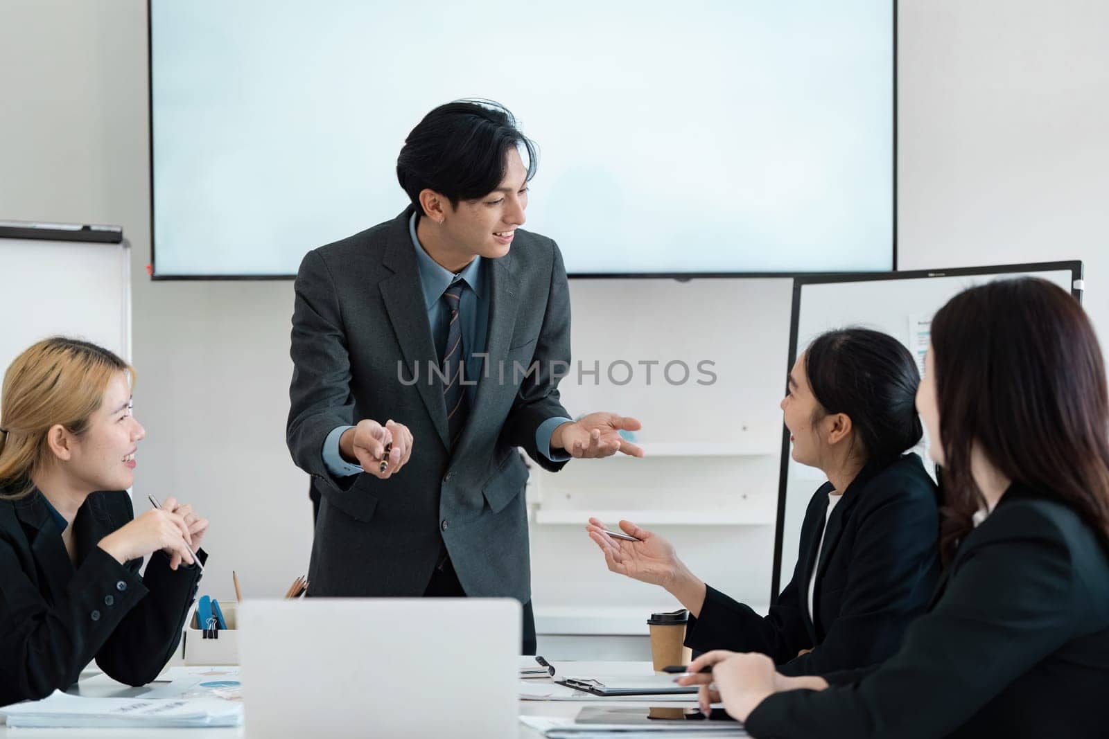 An engaging Asian businessman passionately presents ideas to a diverse team, fostering collaboration and creativity in a contemporary office setting.