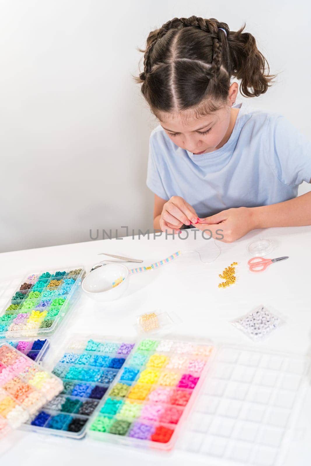 Little girl enjoys crafting colorful bracelets with vibrant clay beads set.