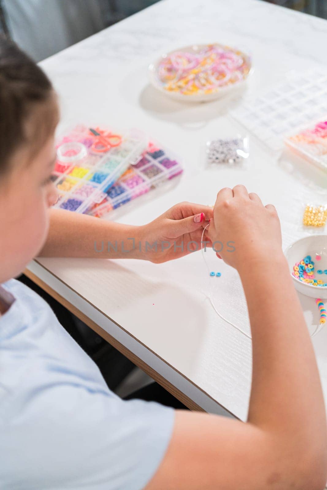 Little girl enjoys crafting colorful bracelets with vibrant clay beads set.
