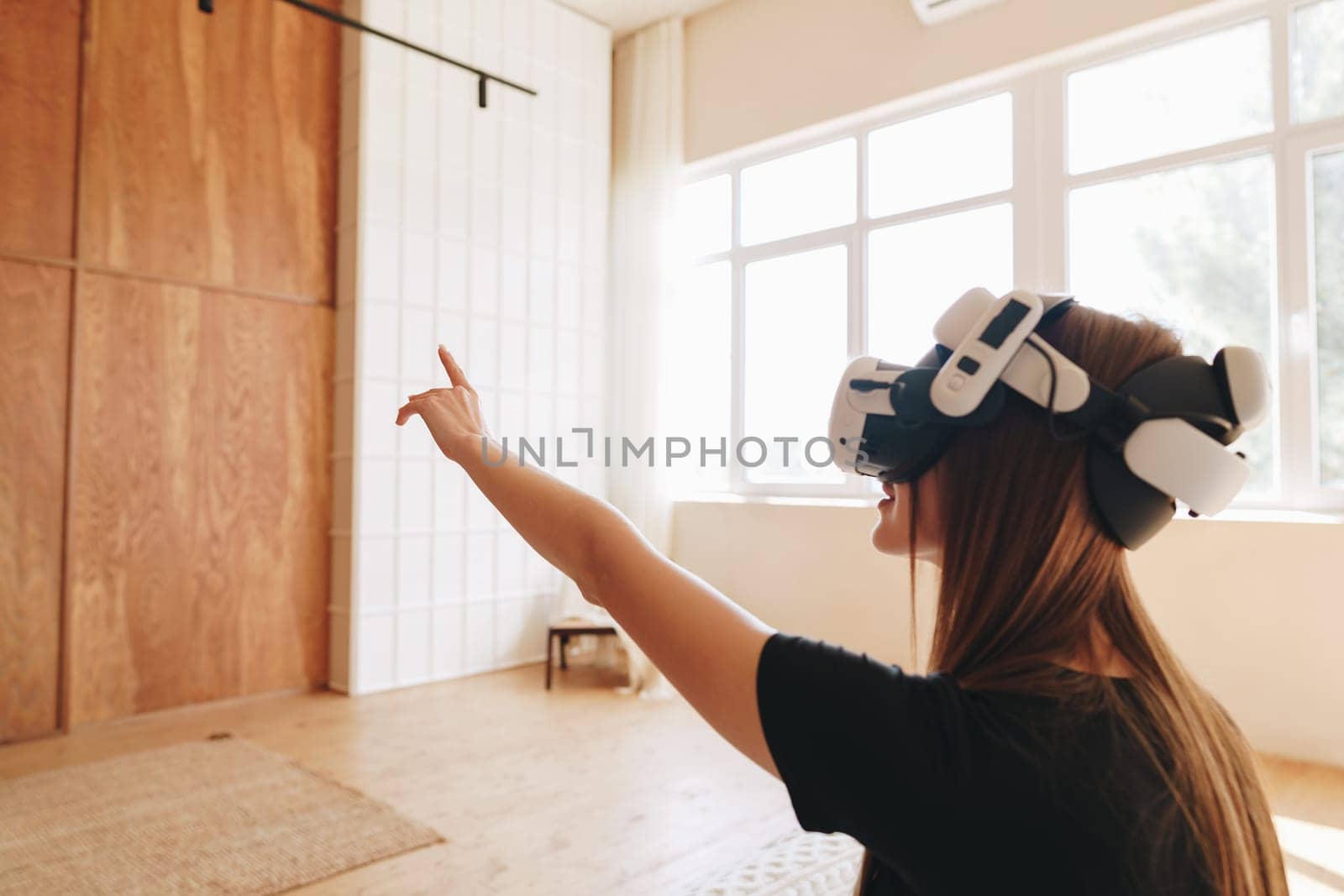 In a modern indoor environment, a woman wearing a virtual reality headset enthusiastically interacts with a virtual world, pointing towards an unseen object while enjoying the immersive experience.