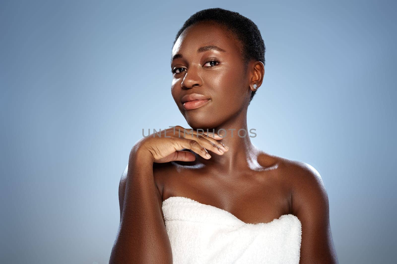 A woman with short hair gracefully poses with her hand near her face, radiating confidence and beauty. The soft blue background enhances her radiant skin tone and charm.