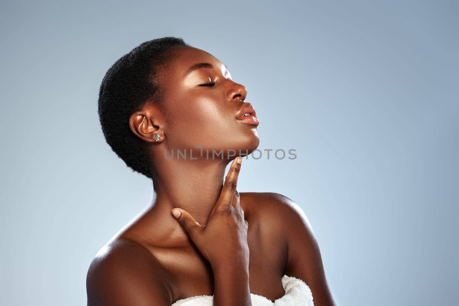 A confident woman with short hair poses against a smooth background, highlighting her radiant skin and elegant demeanor while gently touching her neck in a studio environment.