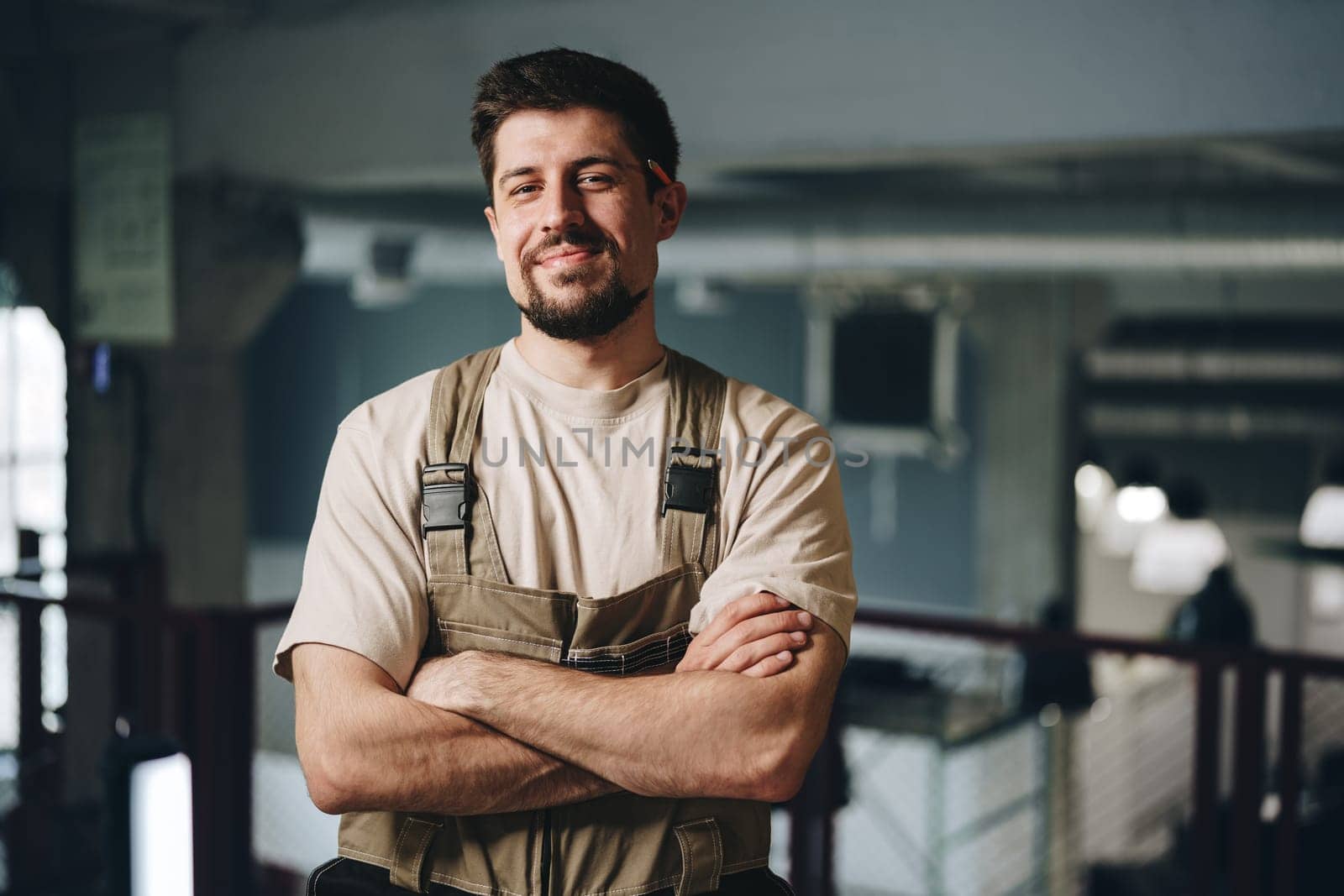 A confident young man in work attire stands with arms crossed in a contemporary indoor environment. Natural light highlights the vibrant workspace, showcasing his professionalism.