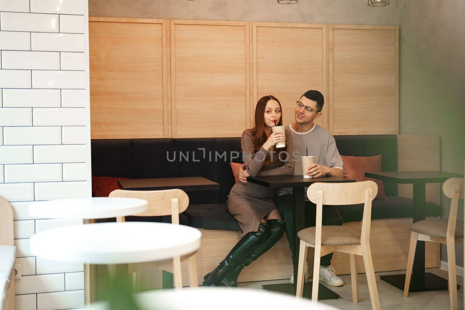 A couple sits together in a contemporary cafe, sipping beverages and engaging in warm conversation. The atmosphere is relaxed and inviting, perfect for a casual outing.