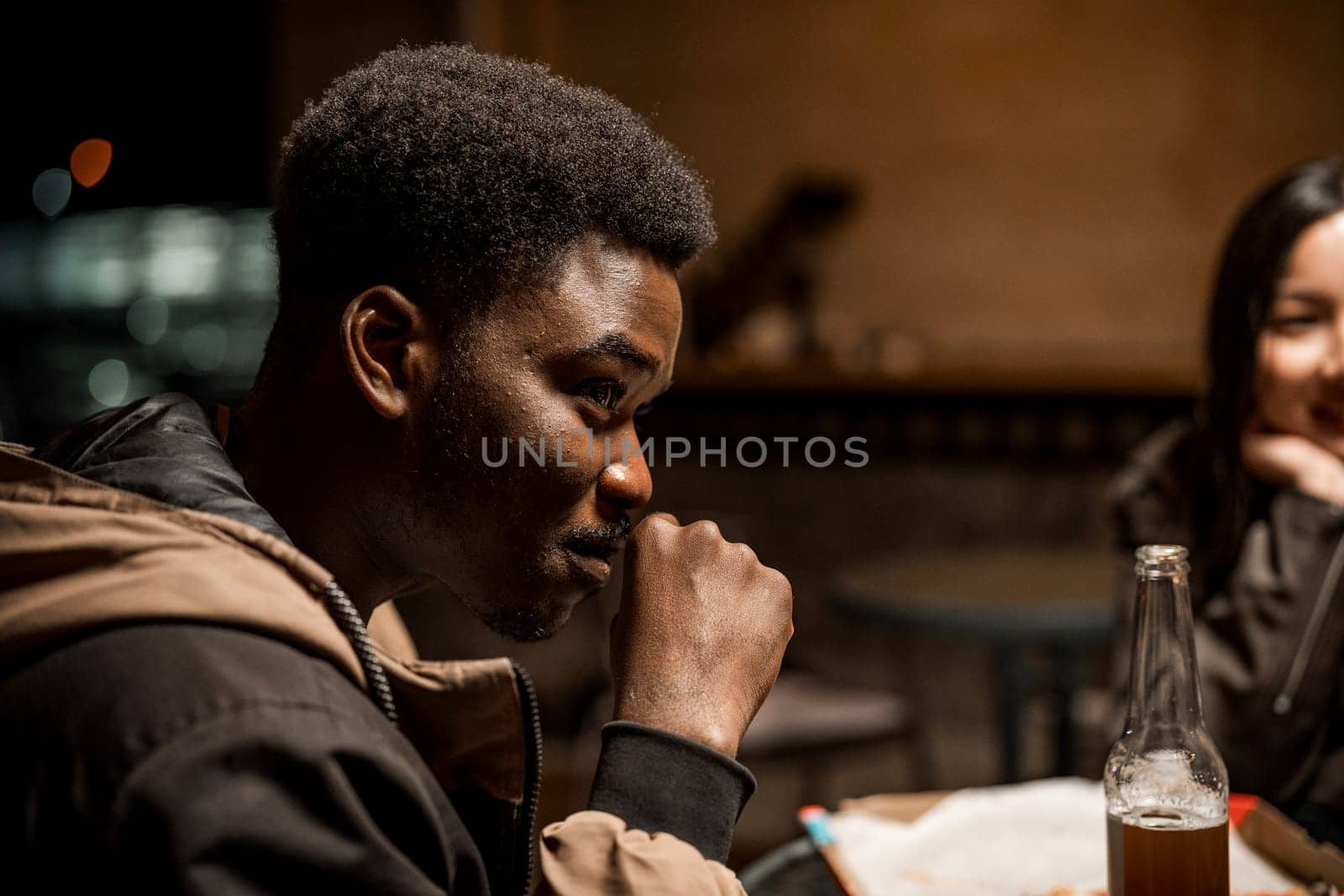 Friends gather in a dimly lit cafe, sharing conversation and laughter. One person enjoys a drink while listening attentively, creating a warm atmosphere.