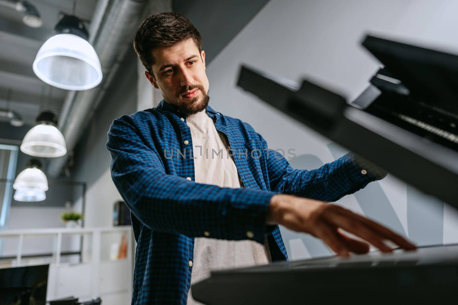 A focused musician plays a keyboard in a contemporary studio environment. Soft light filters through, while the artist deeply engages with the instrument, creating music.