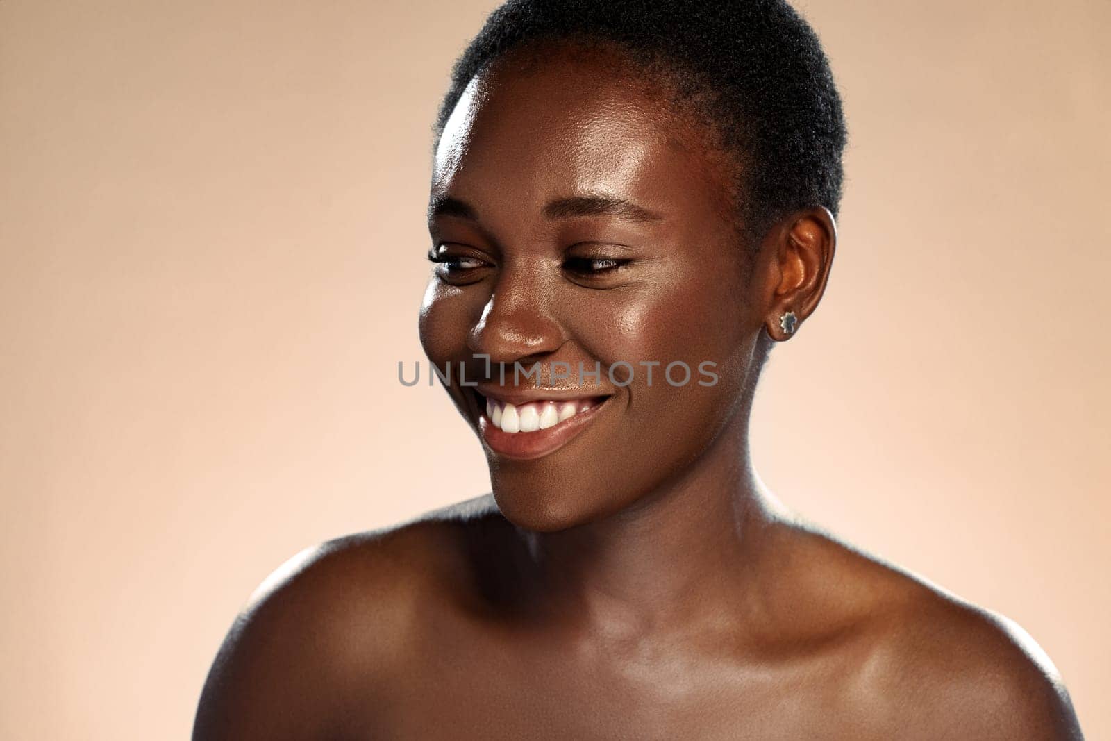 A woman with short, natural hair smiles warmly, exuding confidence and joy. Her skin glows under soft lighting, creating an inviting and uplifting atmosphere.