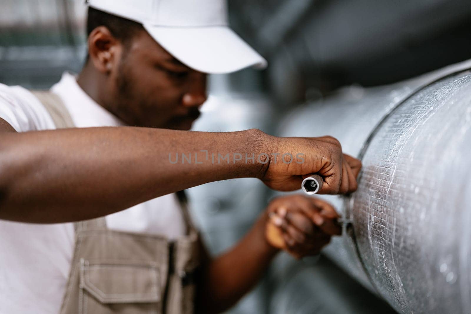 A dedicated professional tightens a pipe connection in a factory setting, showcasing expertise in mechanical repairs and attention to detail during daylight.