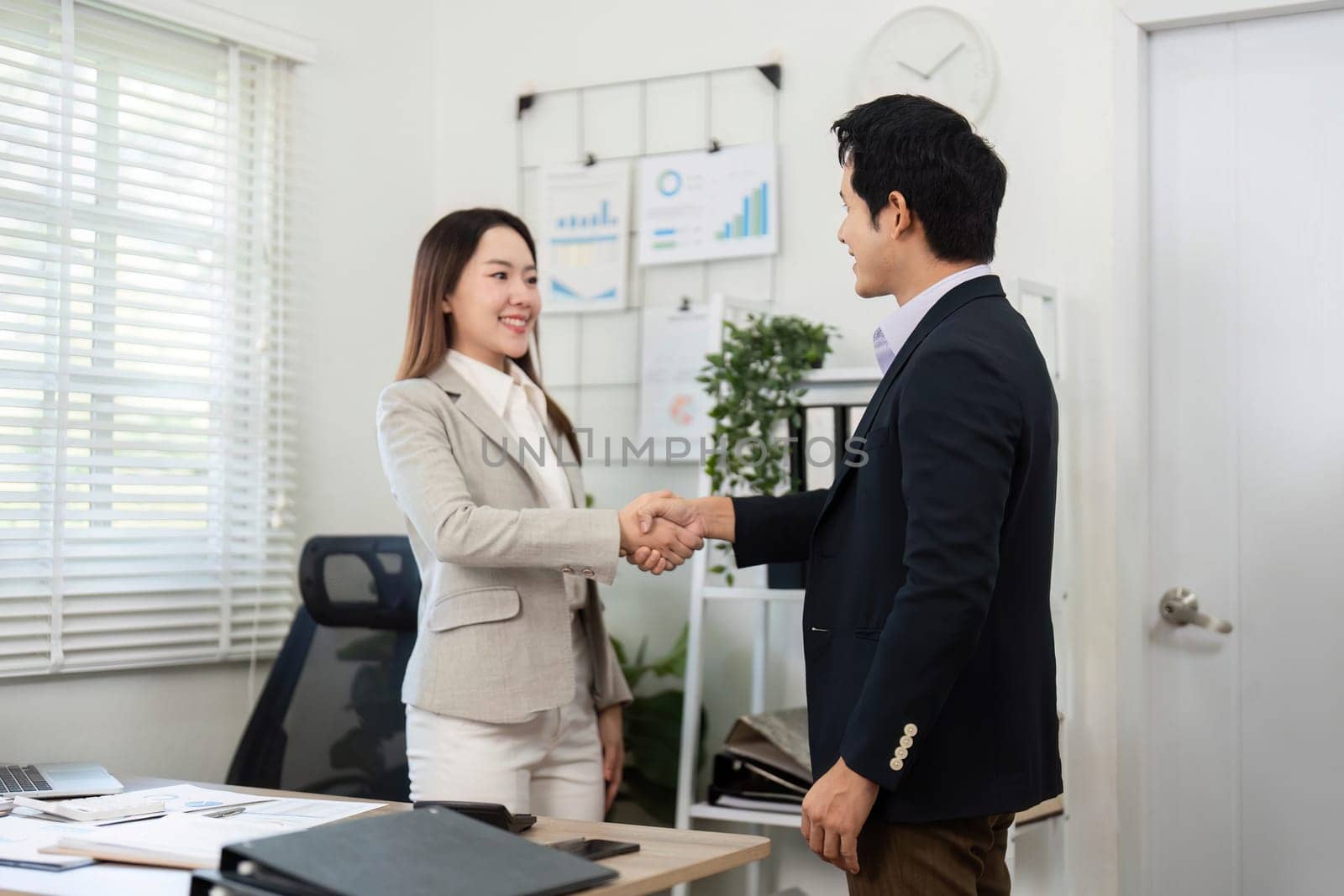 A financial advisor and client shake hands, symbolizing a successful agreement and partnership in a modern office setting.