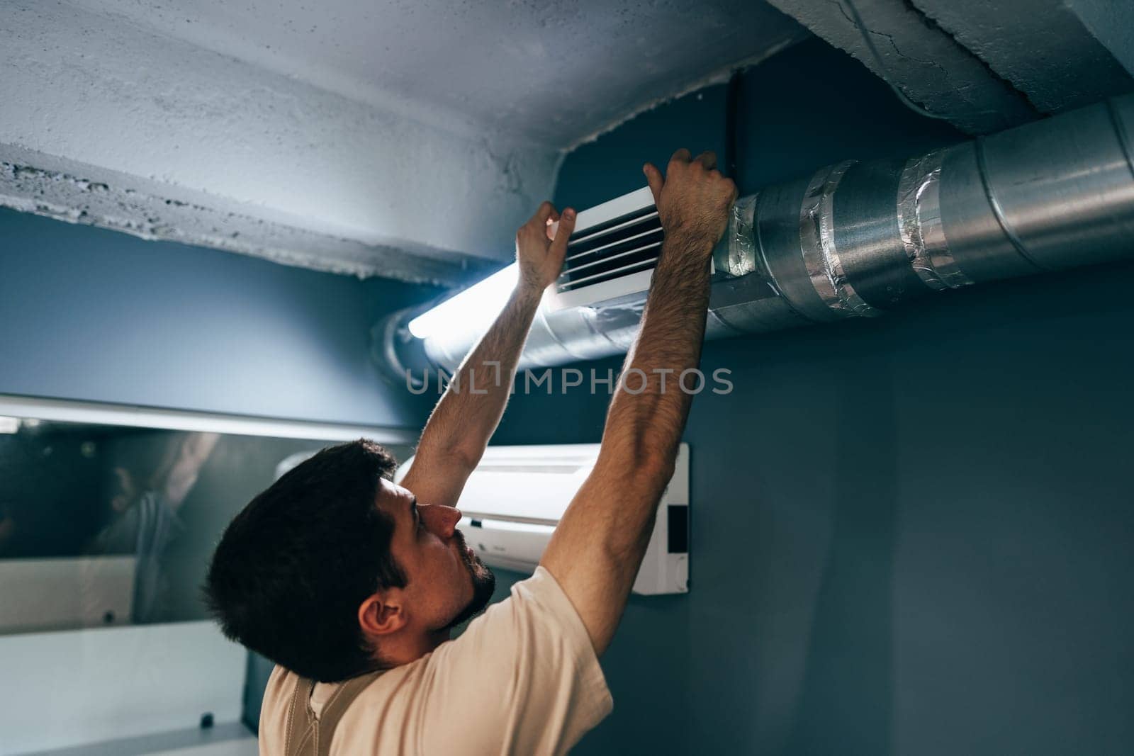 A skilled worker is adjusting the ventilation ducts in a contemporary room. The task is taking place in a well-lit environment, highlighting the importance of air circulation.