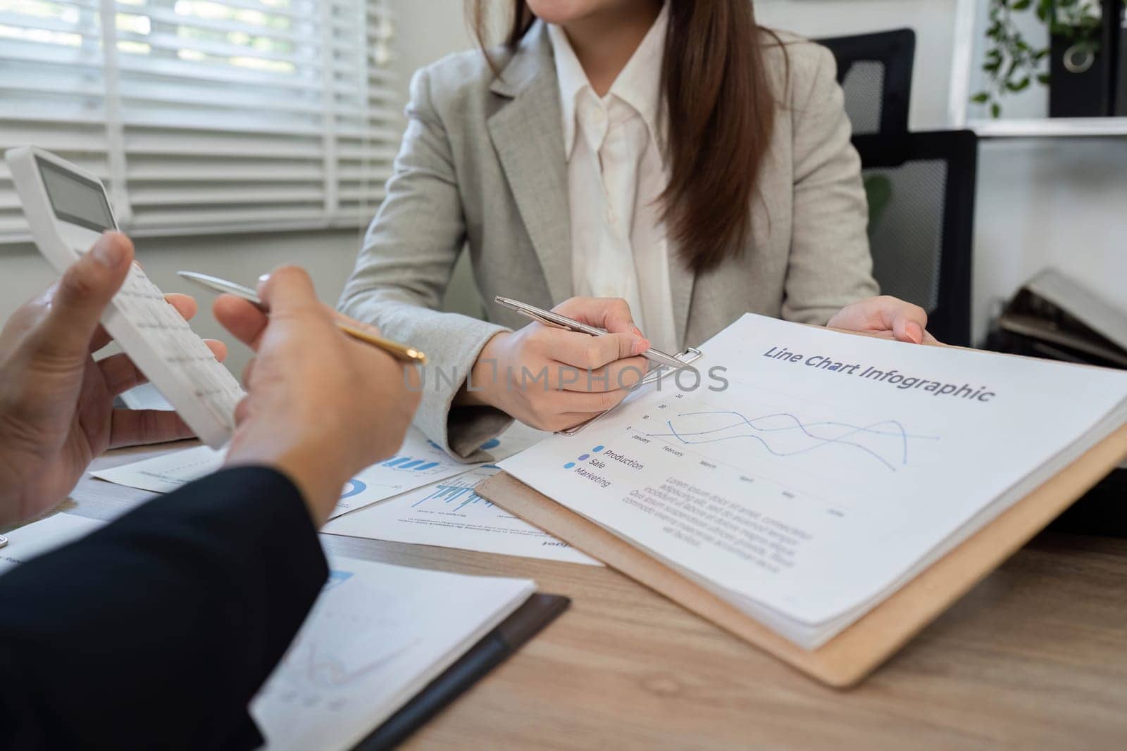 Business professionals analyze financial charts and documents during a consultation, utilizing a calculator for accurate assessments.