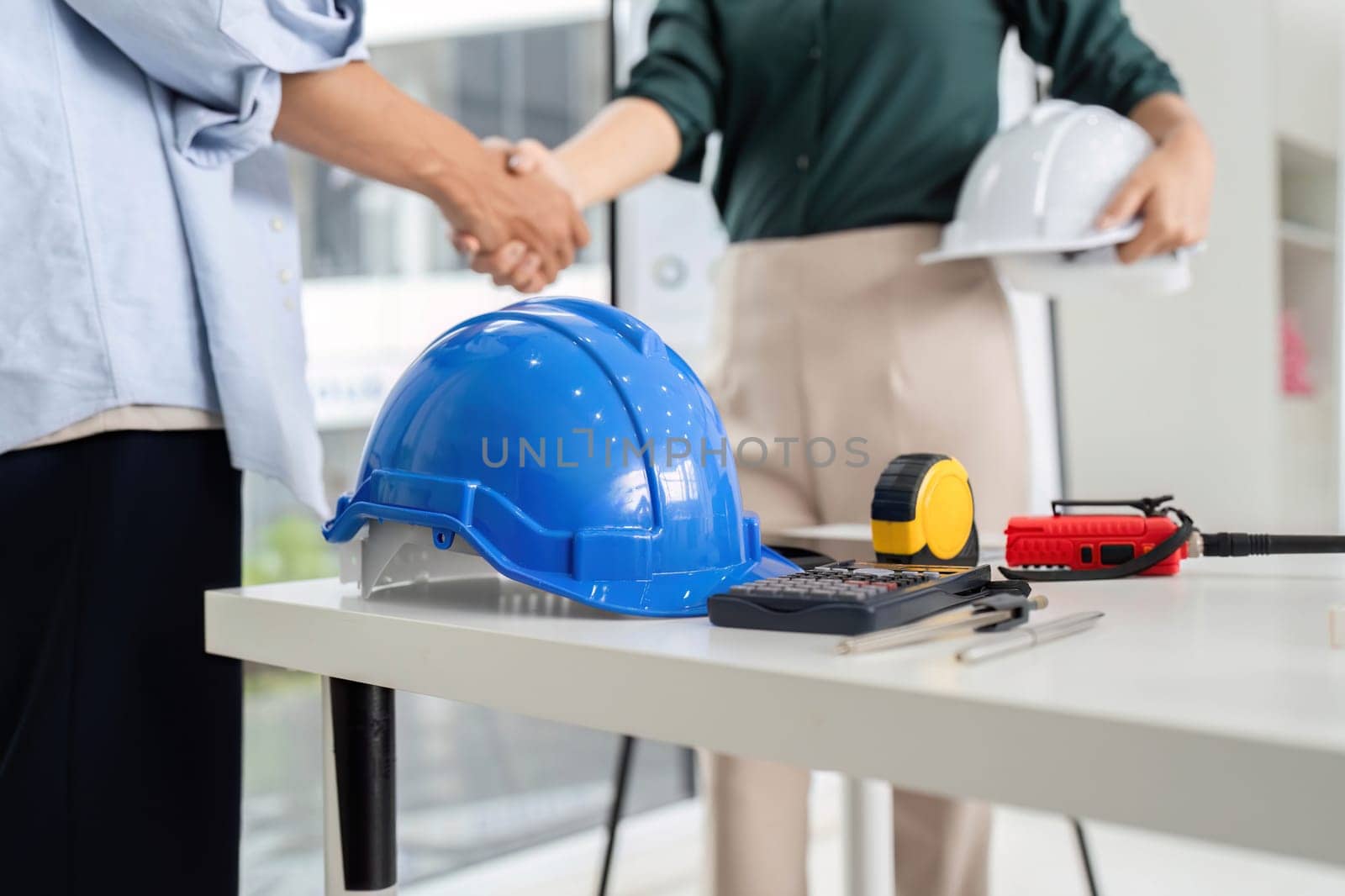 Two professionals shaking hands over a project agreement in a modern office environment. Symbol of partnership and trust.