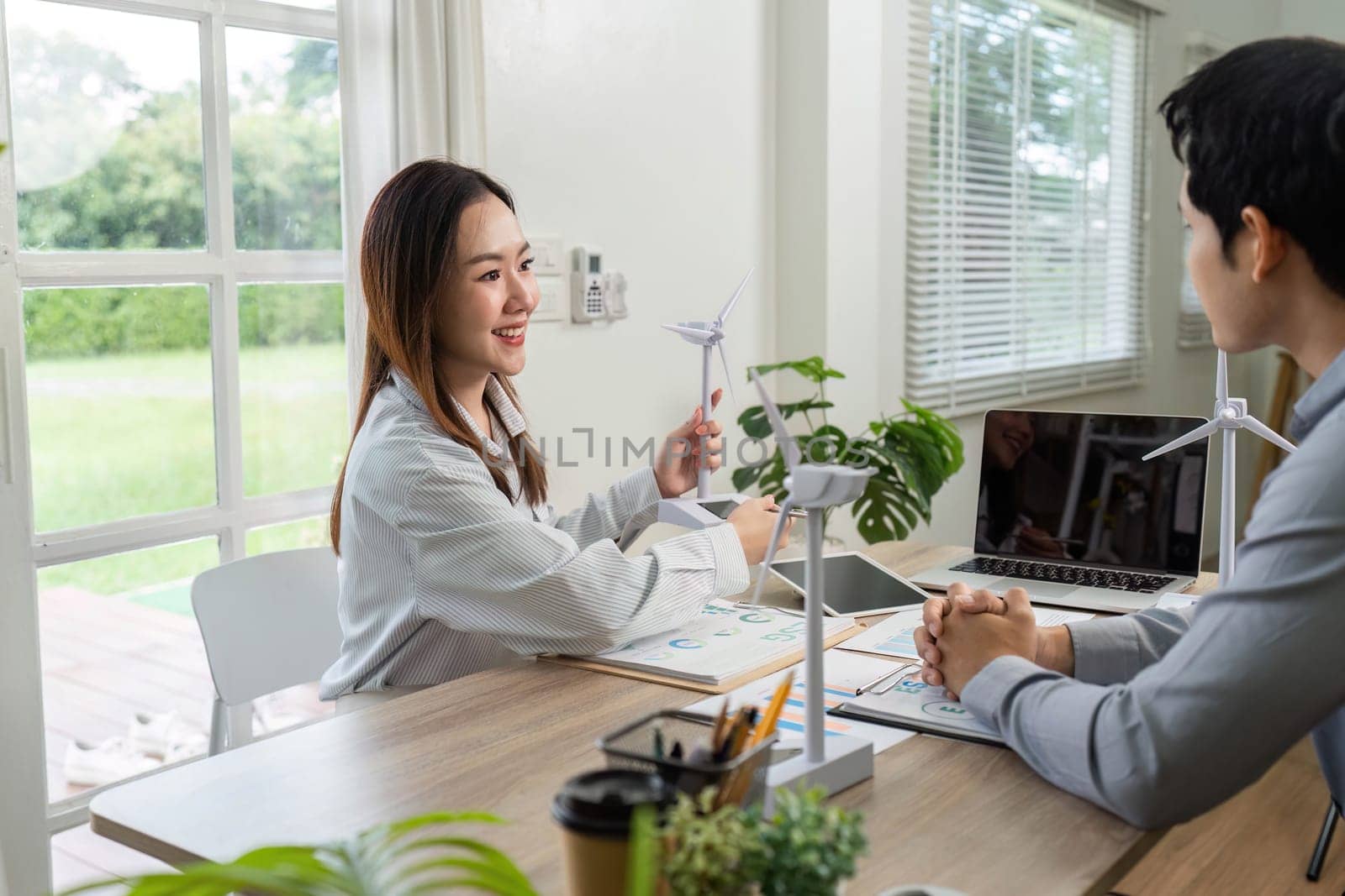 Two business professionals engage in a meeting focused on ESG initiatives, showcasing renewable energy models and data analysis.