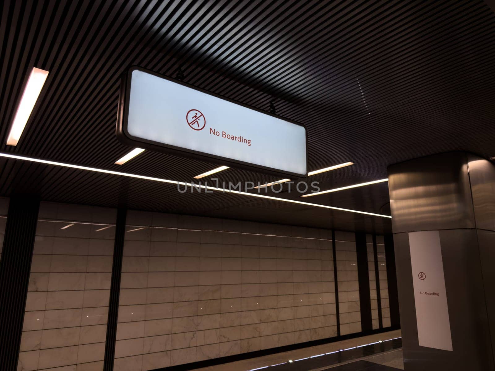 Illuminated No Boarding sign hanging from the ceiling in modern metro station with stylish architectural design. Clear prohibition message ensures passenger safety in public transport zones