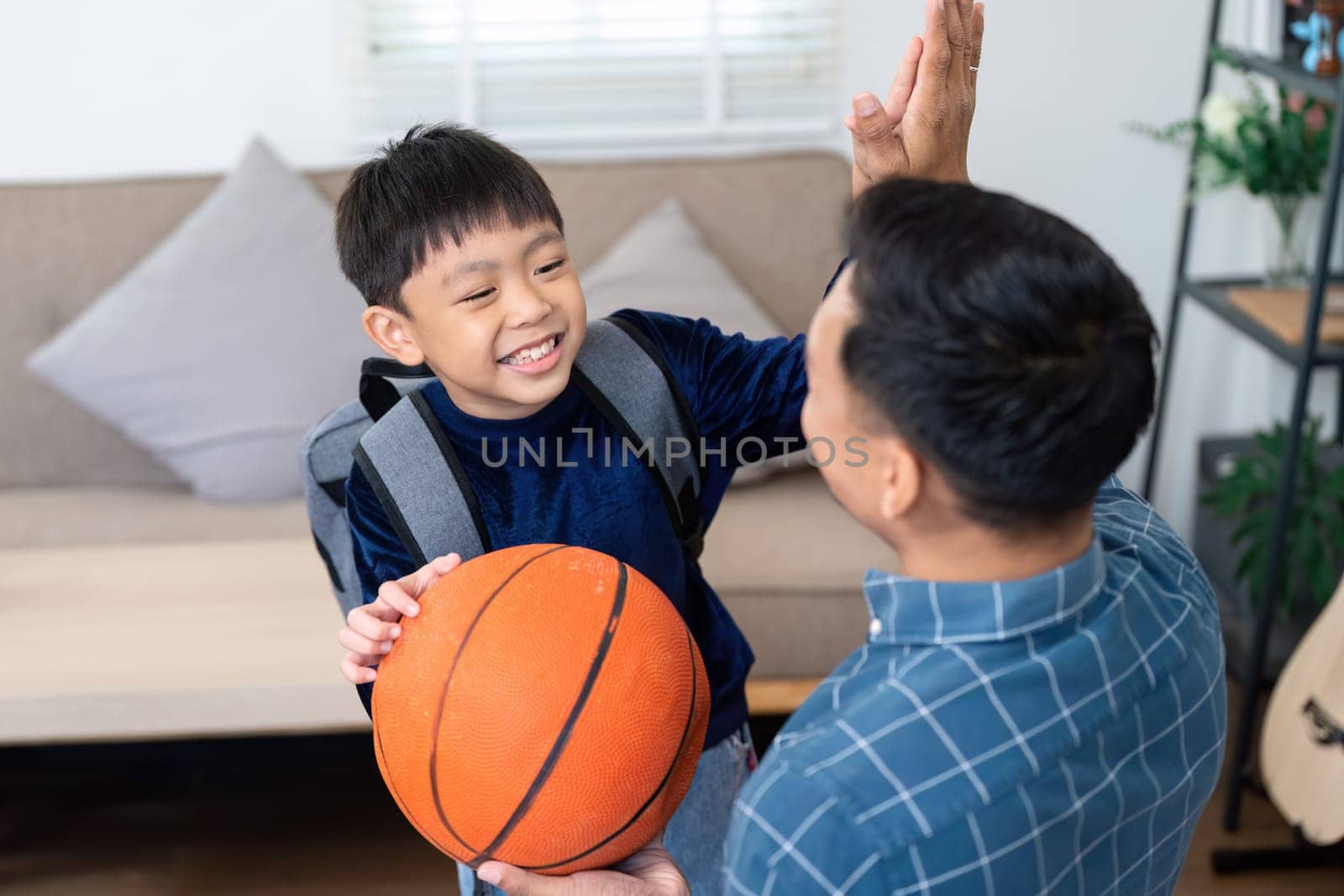 A young boy excitedly greets his father after returning from school, holding a basketball. Their joyful interaction highlights the importance of family support during the back-to-school season.