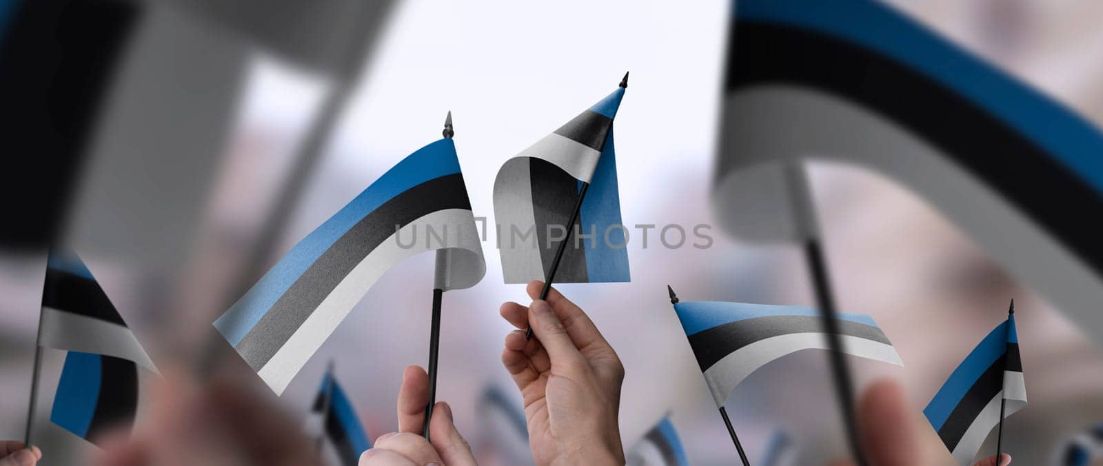 Estonia flags in their hands on a blurred urban background. The photo illustration was created without the use of artificial intelligence, only using Photoshop.