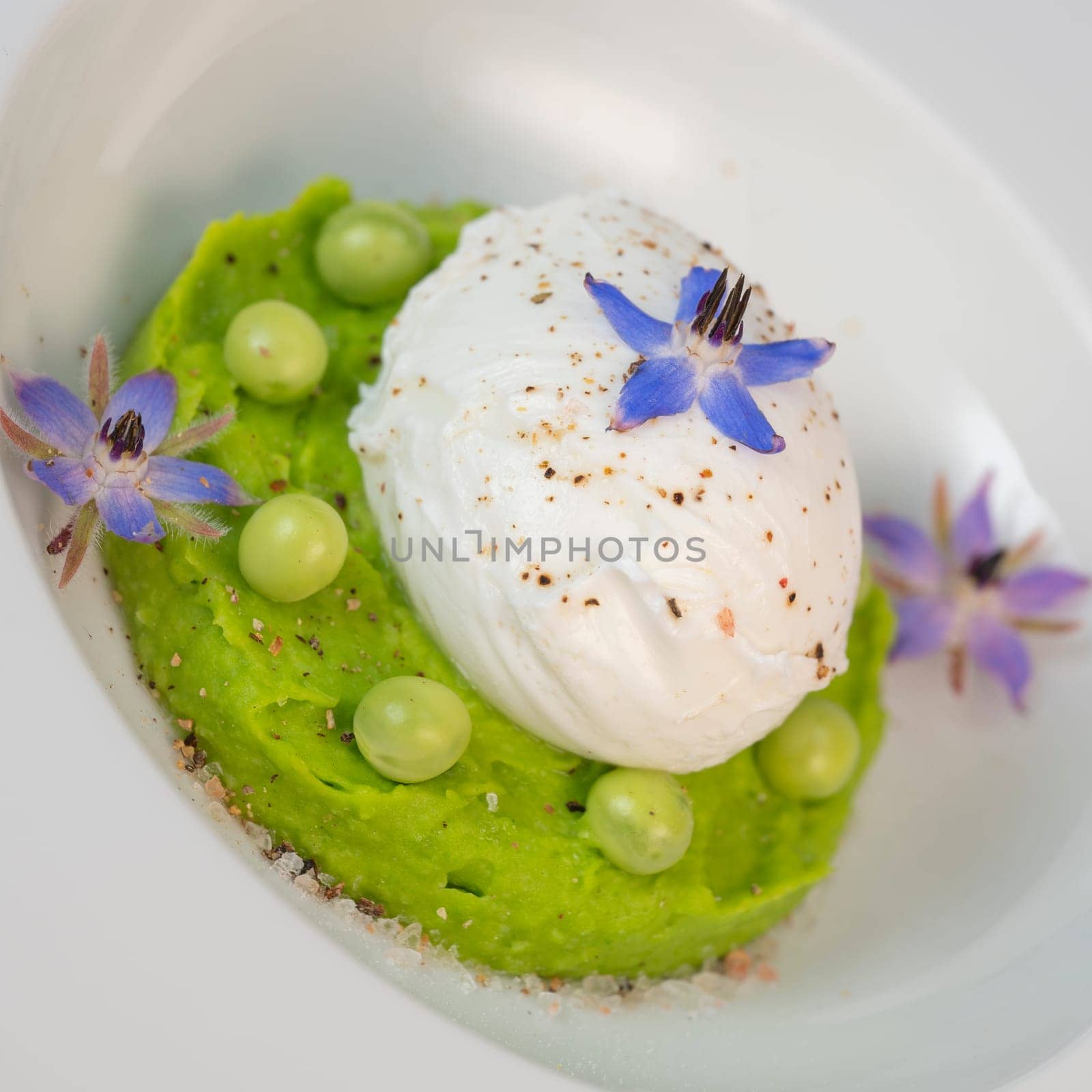 A fresh pea puree is beautifully plated, featuring a poached egg at the center and adorned with borage flowers. The dish showcases vibrant colors and textures, perfect for any spring menu.