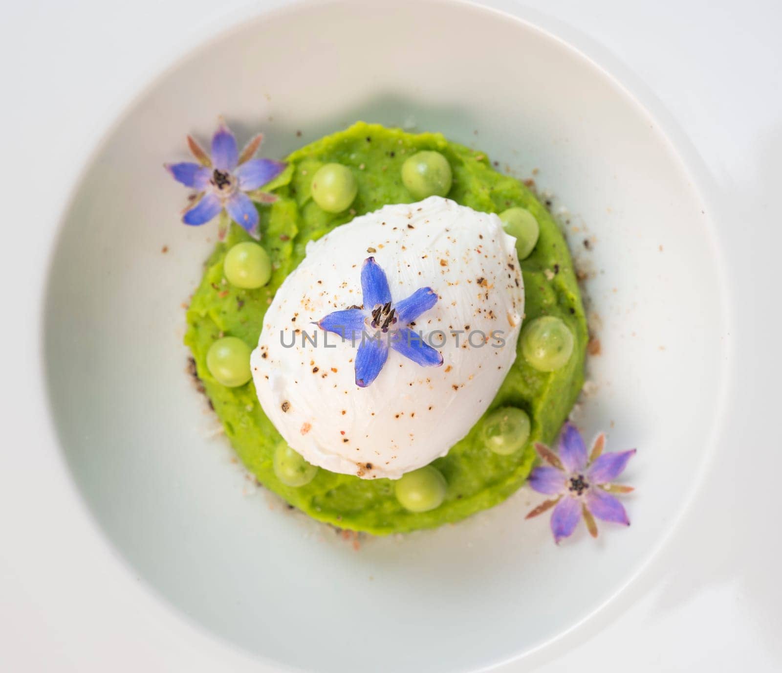 A fresh pea puree is beautifully plated, featuring a poached egg at the center and adorned with borage flowers. The dish showcases vibrant colors and textures, perfect for any spring menu.