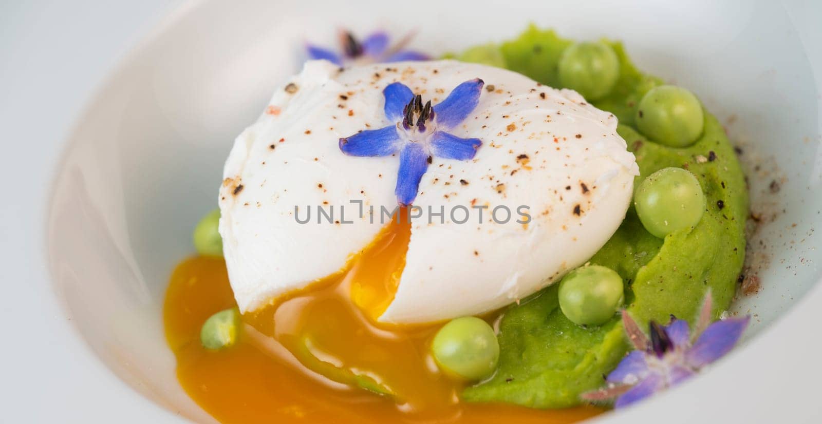 A fresh pea puree is beautifully plated, featuring a poached egg at the center and adorned with borage flowers. The dish showcases vibrant colors and textures, perfect for any spring menu.