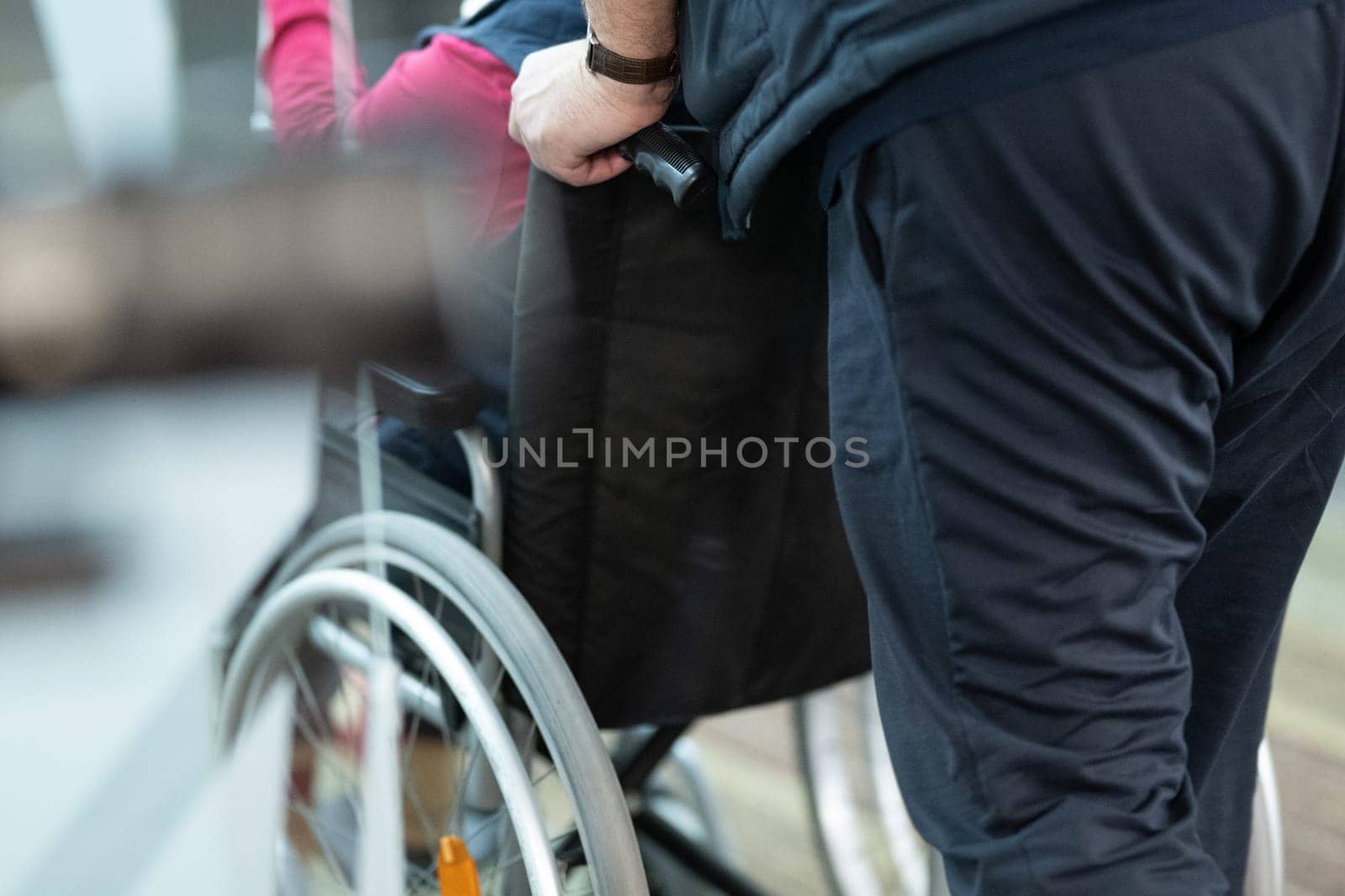 Partial view of a person assisting someone in a wheelchair, showing hands and wheels.